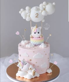 a pink cake decorated with white and gold unicorns, clouds and stars on top