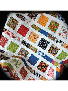 a quilted table topper with colorful squares and flowers on the front, sitting on a chair