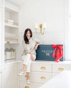 a woman sitting on top of a counter with a box in front of her smiling