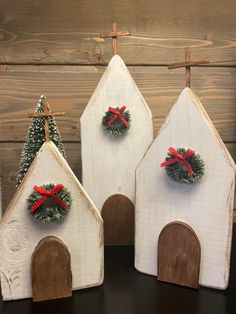 three small wooden houses with wreaths and bows on the front one has a cross