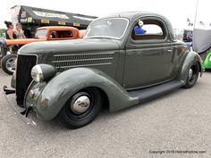 an antique car is parked in a lot with other old cars and people looking at it