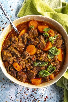 a bowl filled with meat and carrots on top of a green napkin next to a spoon