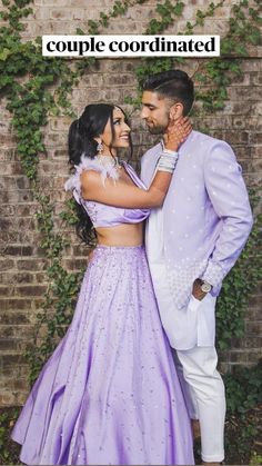 a man and woman standing next to each other in front of a brick wall with ivy growing on it