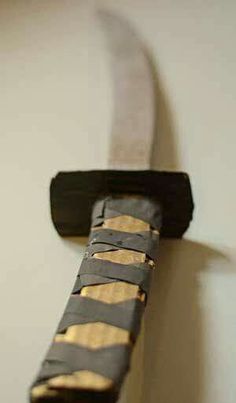 a close up of a knife on a wall with a black handle and gold strips