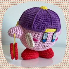 a crocheted toy with a purple hat and red pants