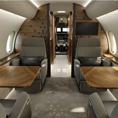 the inside of an airplane with wooden tables and leather seats on each side, facing towards the front door