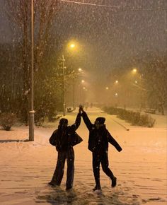 two people standing in the snow with their arms up and one person holding an umbrella