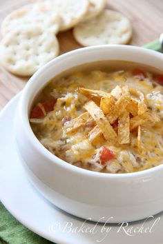 a close up of a bowl of soup with cheese and tortilla chips on the side