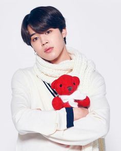 a young man holding a red teddy bear in his arms while wearing a white sweater