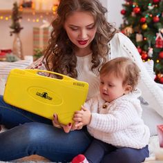 a woman sitting on the floor playing with a child in front of a christmas tree