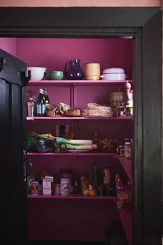 an open pantry door with food and drinks on the shelves in front of purple walls