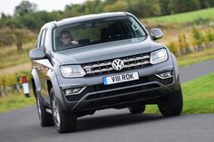 a grey vw atlas pickup driving down a country road with grass and trees in the background