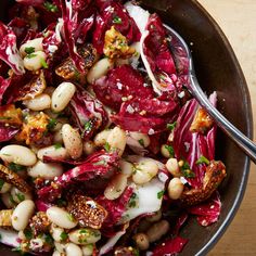 a bowl filled with red cabbage, beans and other food on top of a wooden table