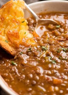 a spoon in a bowl filled with chili and cheese soup next to a piece of bread