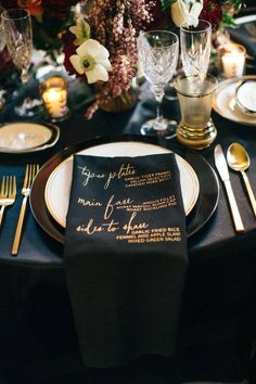 a black and gold wedding table setting with napkins, silverware, and flowers