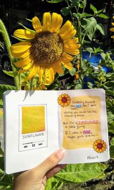 someone is holding up a sunflower in front of some green plants with yellow flowers