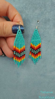 a pair of colorful beaded earrings being held by a person's hand on a blue background