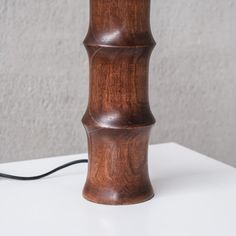 a wooden lamp on a white table with a black cord plugged in to it