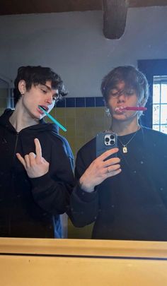 two young men standing in front of a mirror brushing their teeth