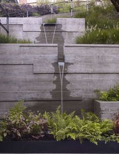 a water fountain in the middle of a garden with plants growing on it's sides