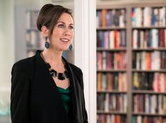 a woman standing in front of a book shelf filled with books and wearing large earrings