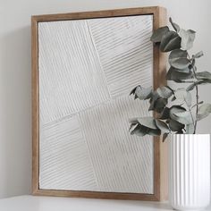 a white vase sitting on top of a table next to a wooden framed wall mirror