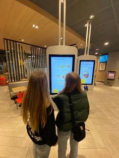 two young women standing in front of large televisions