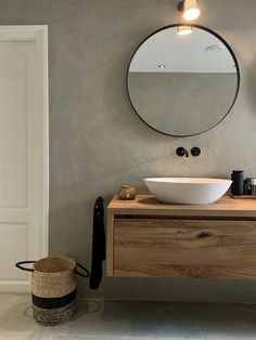 a bathroom with a round mirror above the sink and a wooden cabinet below that has a basket on it