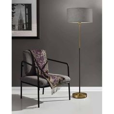 the floor lamp is next to a chair with a blanket on it and a rug