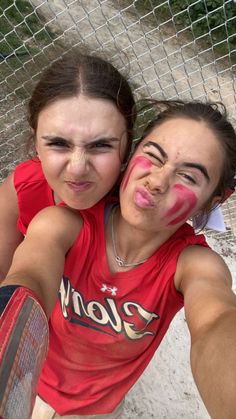 two girls with their faces painted in pink and white, posing for the camera behind a fence