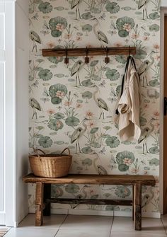 a wooden bench sitting next to a wall covered in floral wallpaper and hanging hooks