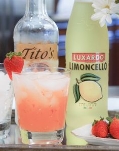 a glass with ice and strawberries next to two bottles of limooncello