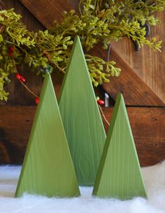 three green wooden christmas trees sitting on top of a white fur covered floor next to a tree