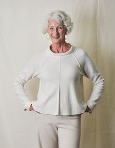 an older woman standing with her hands on her hips, wearing white pants and a sweater