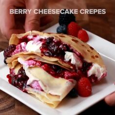 two crepes on a plate with berries and whipped cream in the middle, being held by someone's hand