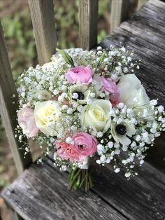 a bouquet of white and pink flowers sitting on top of a wooden bench with baby's breath