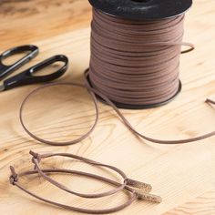 a spool of thread next to scissors on a wooden table with brown cords and pliers