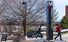 two people walking on the sidewalk in front of a sign