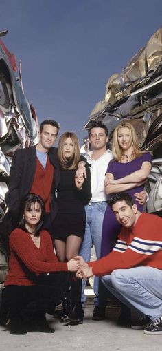 the cast of friends posing in front of a pile of junk