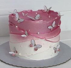 there is a pink and white cake with butterflies on the top, sitting on a plate