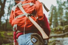 a man with a red backpack is walking through the woods carrying a large wooden stick