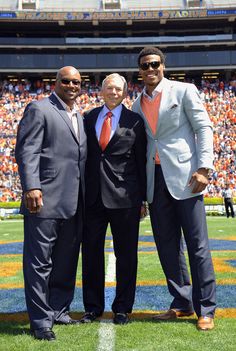 two men and one man are standing on the field in front of an audience at a football game