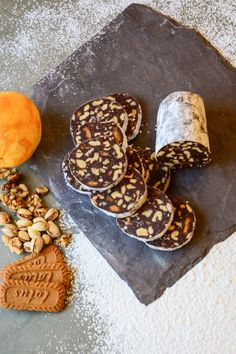 an assortment of cookies and nuts on a slate platter next to some oranges