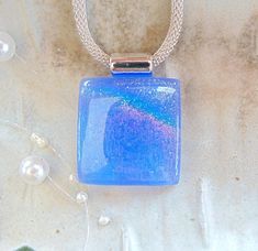 The glass stone in this beautiful pendant measures approximately 1 1/16" square and has a large silver plated tube style bail attached.  The dichroic glass in this pendant shimmers with blue and a rainbow on white glass.  It is capped with clear and full fused for depth and strength.   The matching earrings can be found by clicking here.   https://www.etsy.com/listing/1809179247/blue-earrings-rainbow-dichroic-glass?click_key=4646d955a821fcdf31d86b65dccbfe8314533c6f%3A1809179247&click_sum=f4aaf6e Dichroic Jewelry, Mesh Necklace, Dichroic Glass Pendant, Fused Glass Jewelry, Snake Necklace, Dichroic Glass, Blue Necklace, Blue Earrings, Glass Jewelry