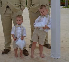 two young boys dressed in formal clothes standing next to each other on the beach with their parents