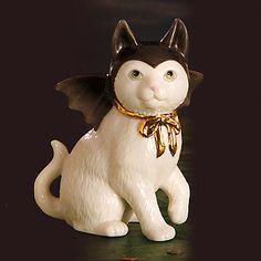 a white cat figurine sitting on top of a green surface with a gold ribbon around it's neck