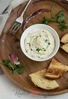 a wooden plate topped with two slices of bread and a bowl of dip