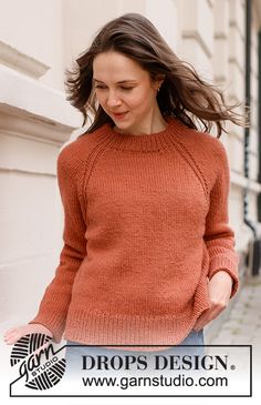 a woman in an orange sweater is walking down the street with her hair blowing in the wind