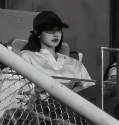 a woman sitting in a chair with a baseball cap on her head and holding a bat