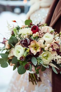 a bridal holding a bouquet of flowers and greenery in the snow on a wedding day